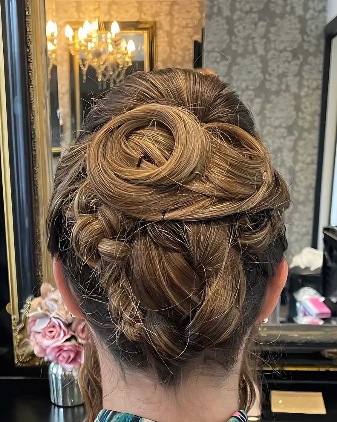 Pinned updo in light brown hair with a rolled swirl at the crown above a small plait, seen from behind