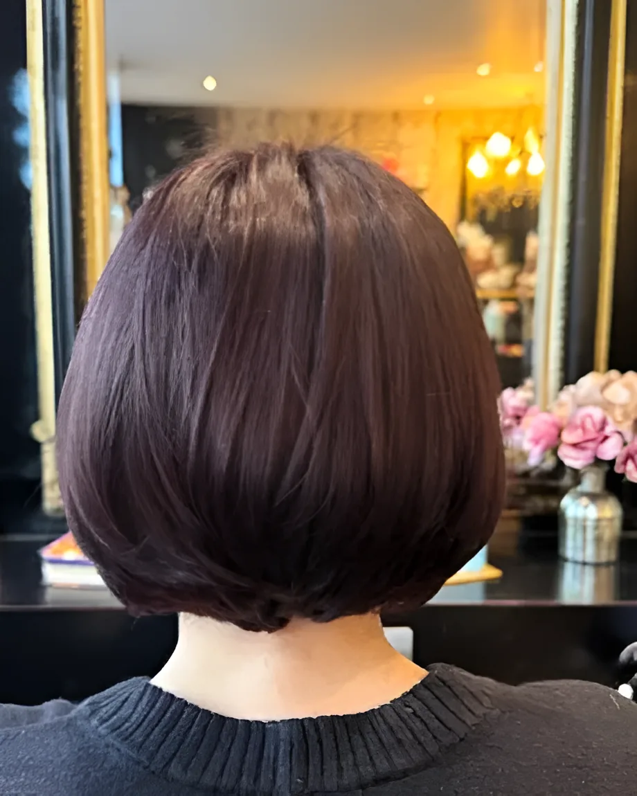 Chin-length bob in a deep plum brown in the salon chair, with a gilt mirror and pink flowers behind