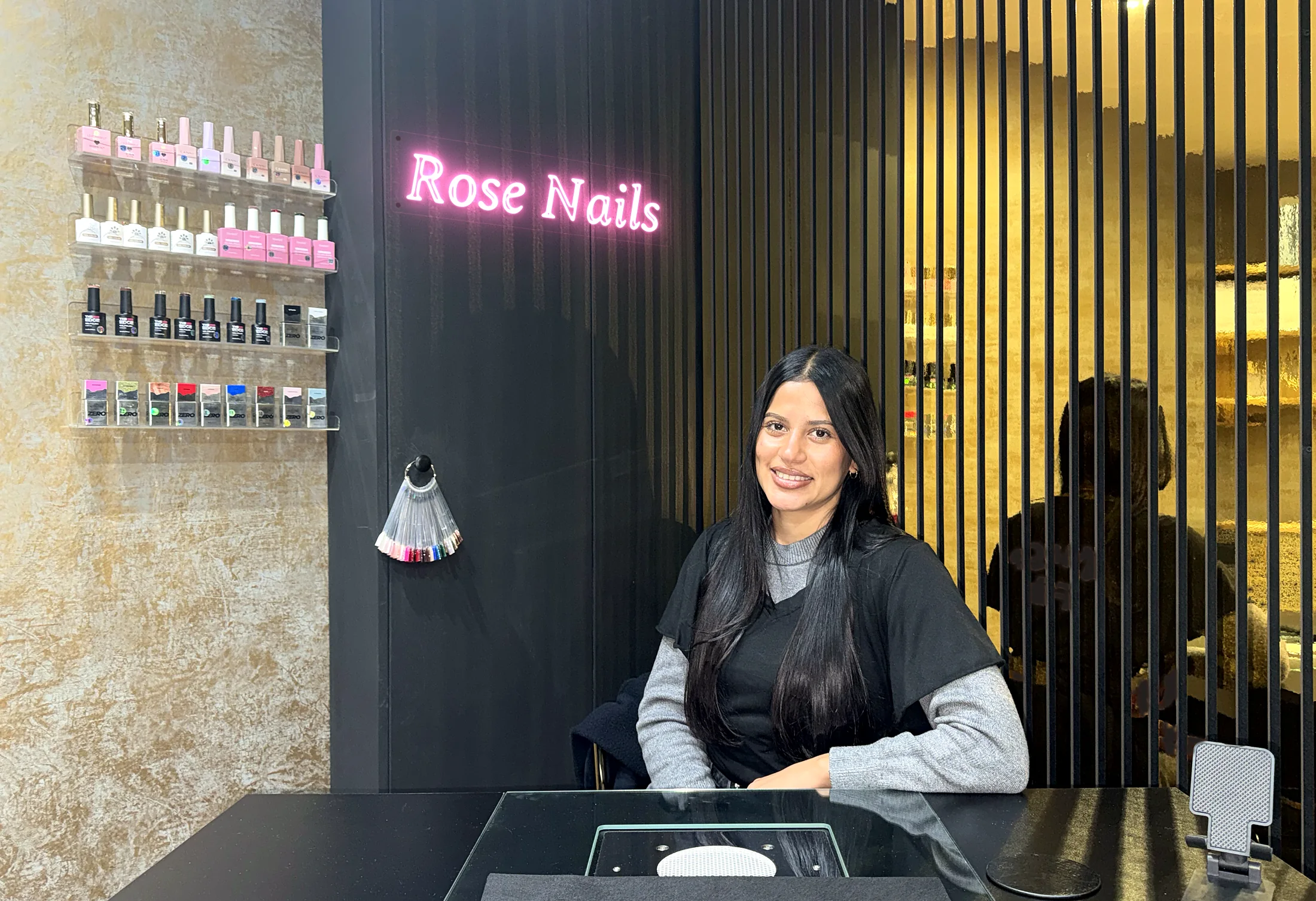 Nem at her nail desk in the Rose Nails studio at Village Flair, with the Rose Nails neon sign on the wall
